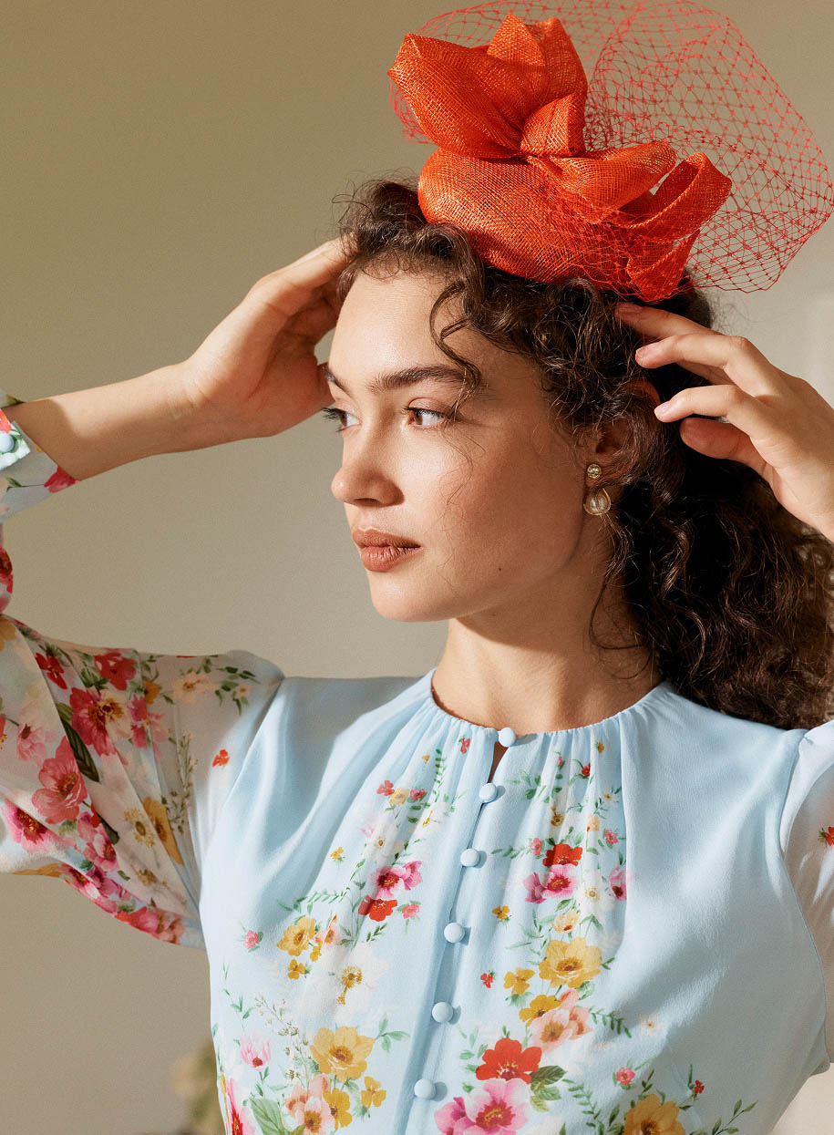 A woman wearing a tomato red fascinator and silk floral dress