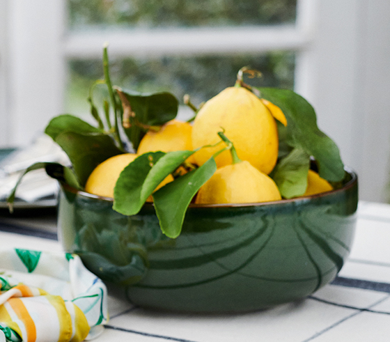 A jug of homemade lemonade, bowl of fresh lemons and a silk scarf sit atop a table.