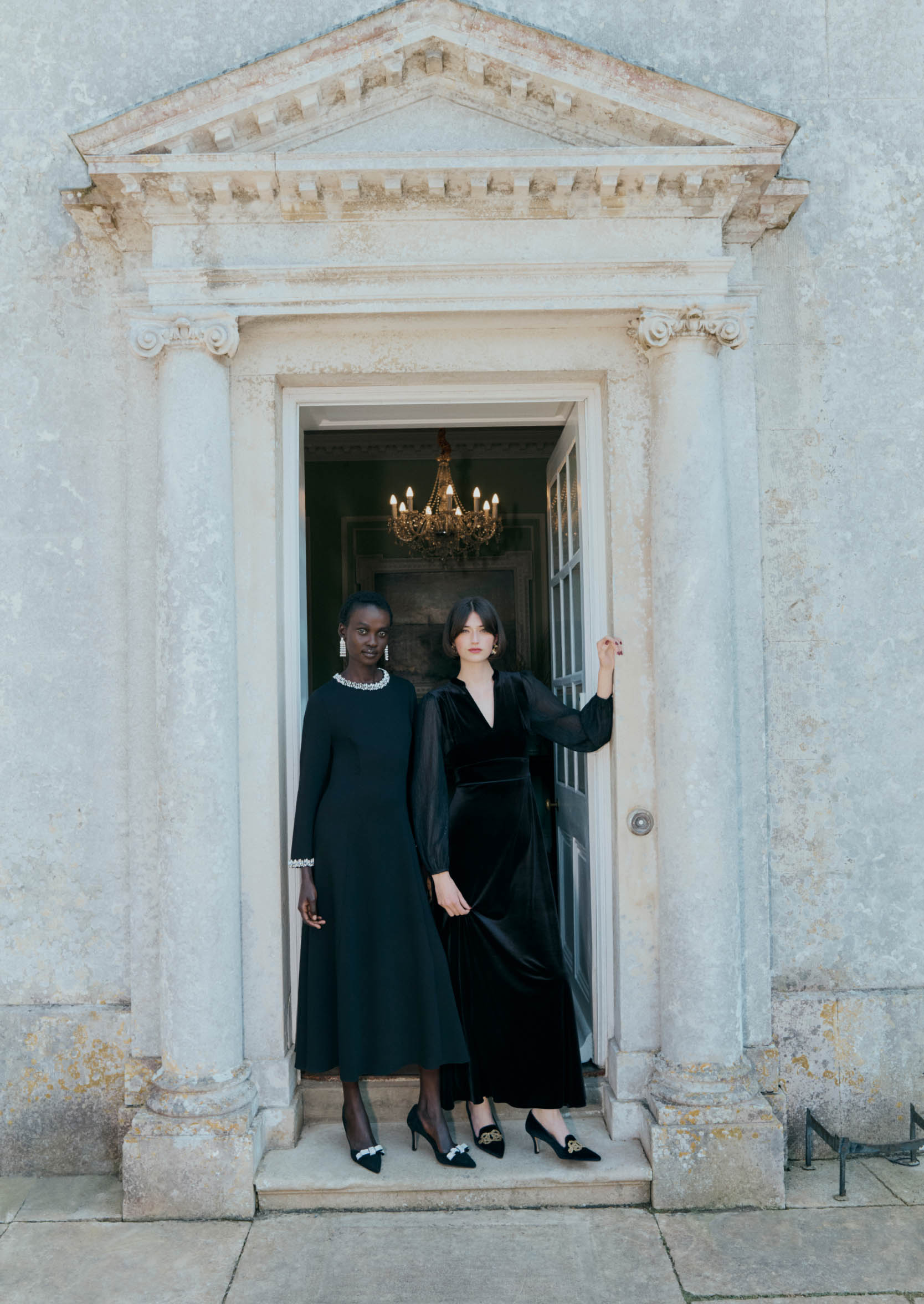 An image of two models standing in a doorway wearing black occasion dresses.